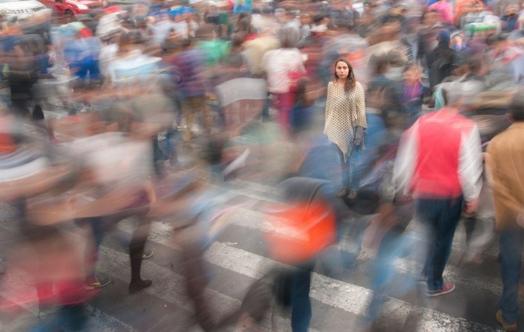 Belebte Kreuzung mit verwischten Passanten und einer stillstehenden Frau