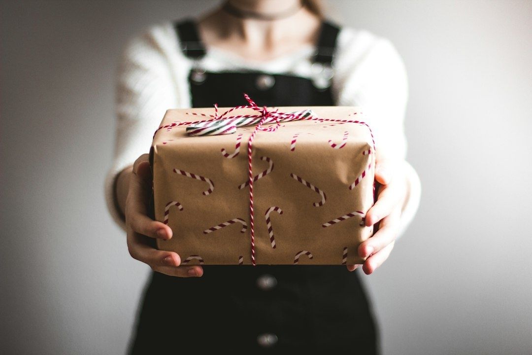 Person hält ein weihnachtlich verpacktes Geschenk mit Schleife in den Händen